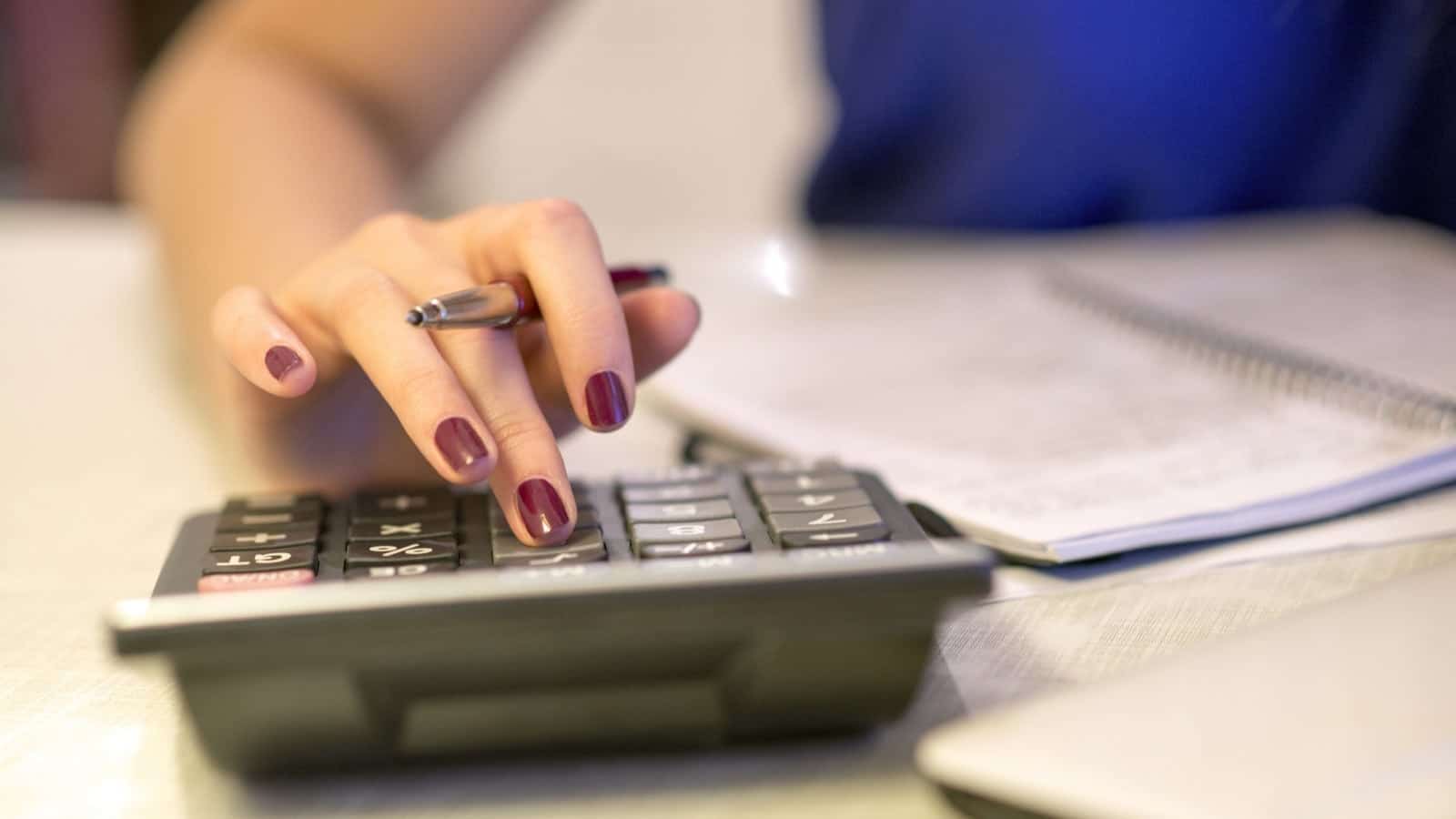 Woman Using Calculator At Desk Stock Photo